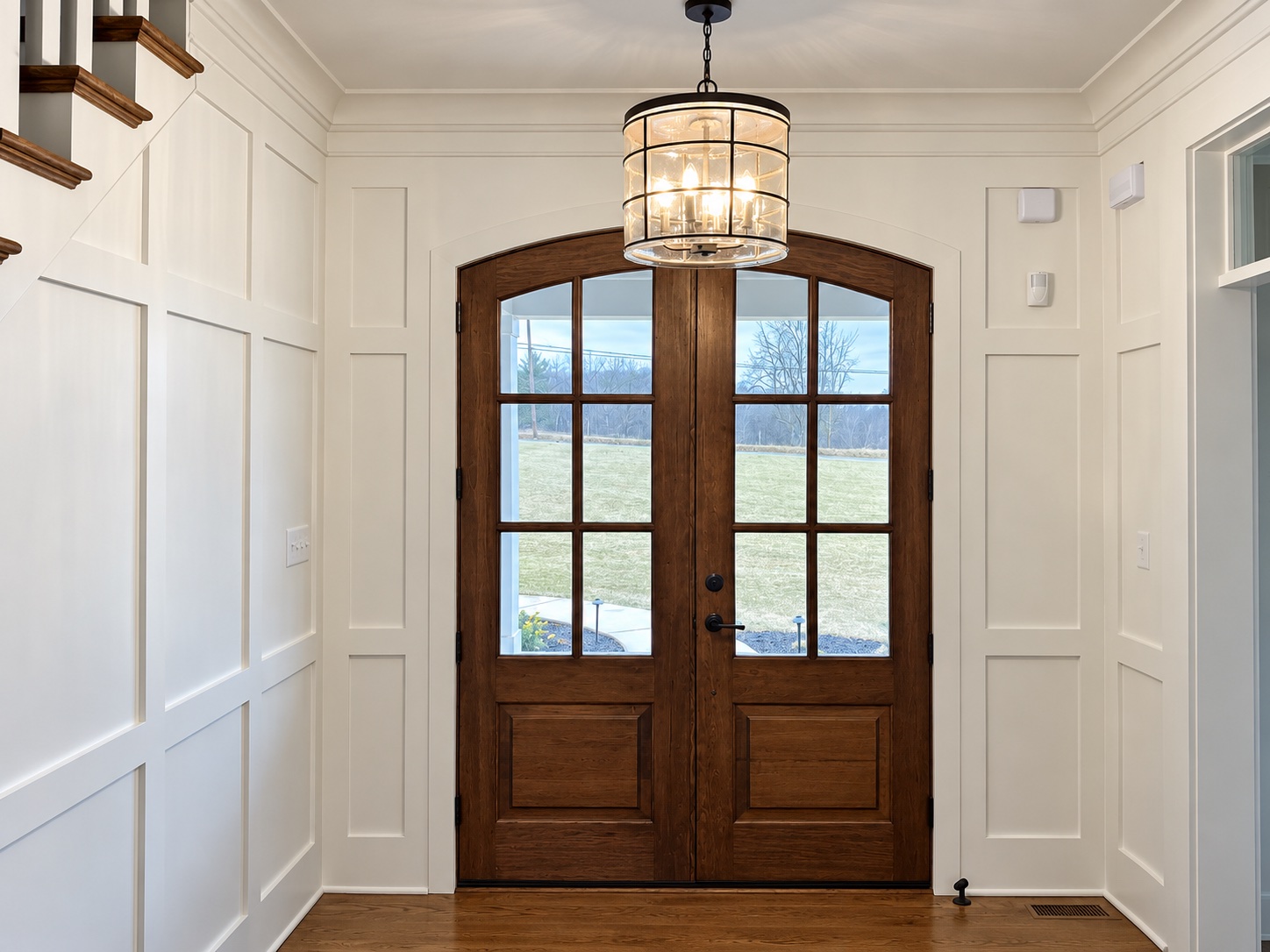 Arched wood double doors surrounded by detailed white wall paneling and crown molding